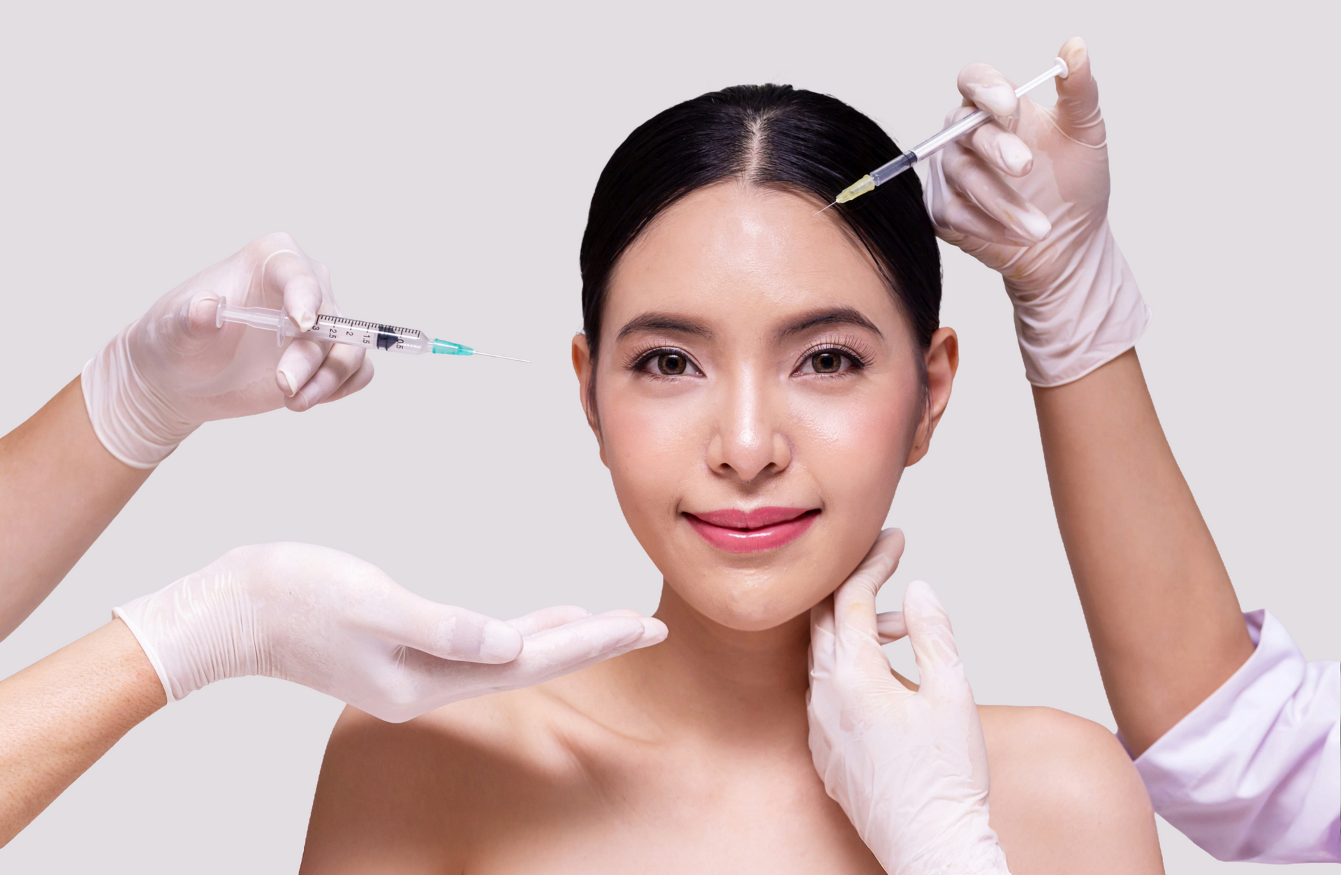Woman receiving cosmetic injections. Hands in gloves hold syringes, examining face. Neutral background.