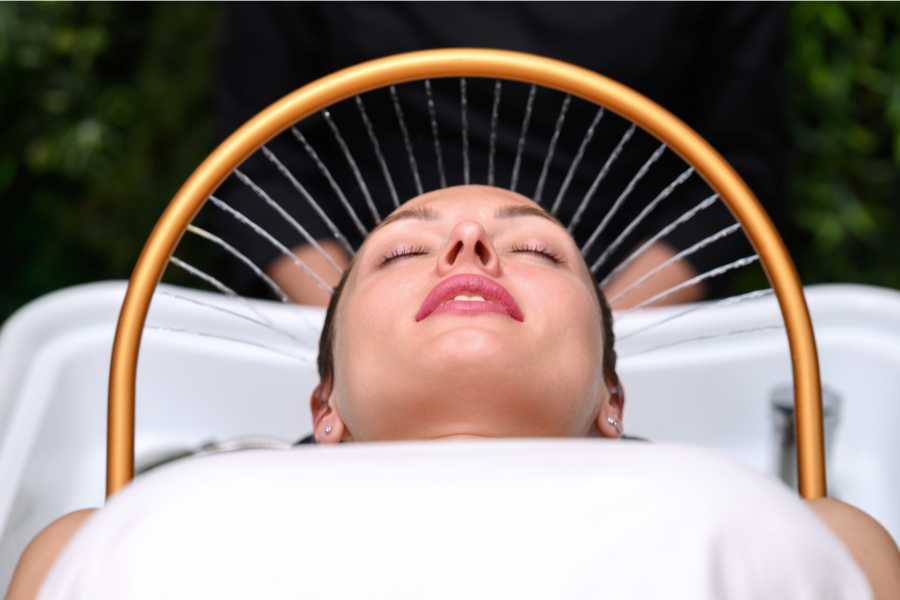 Woman relaxing with water spraying over her face from a golden arch in a salon.