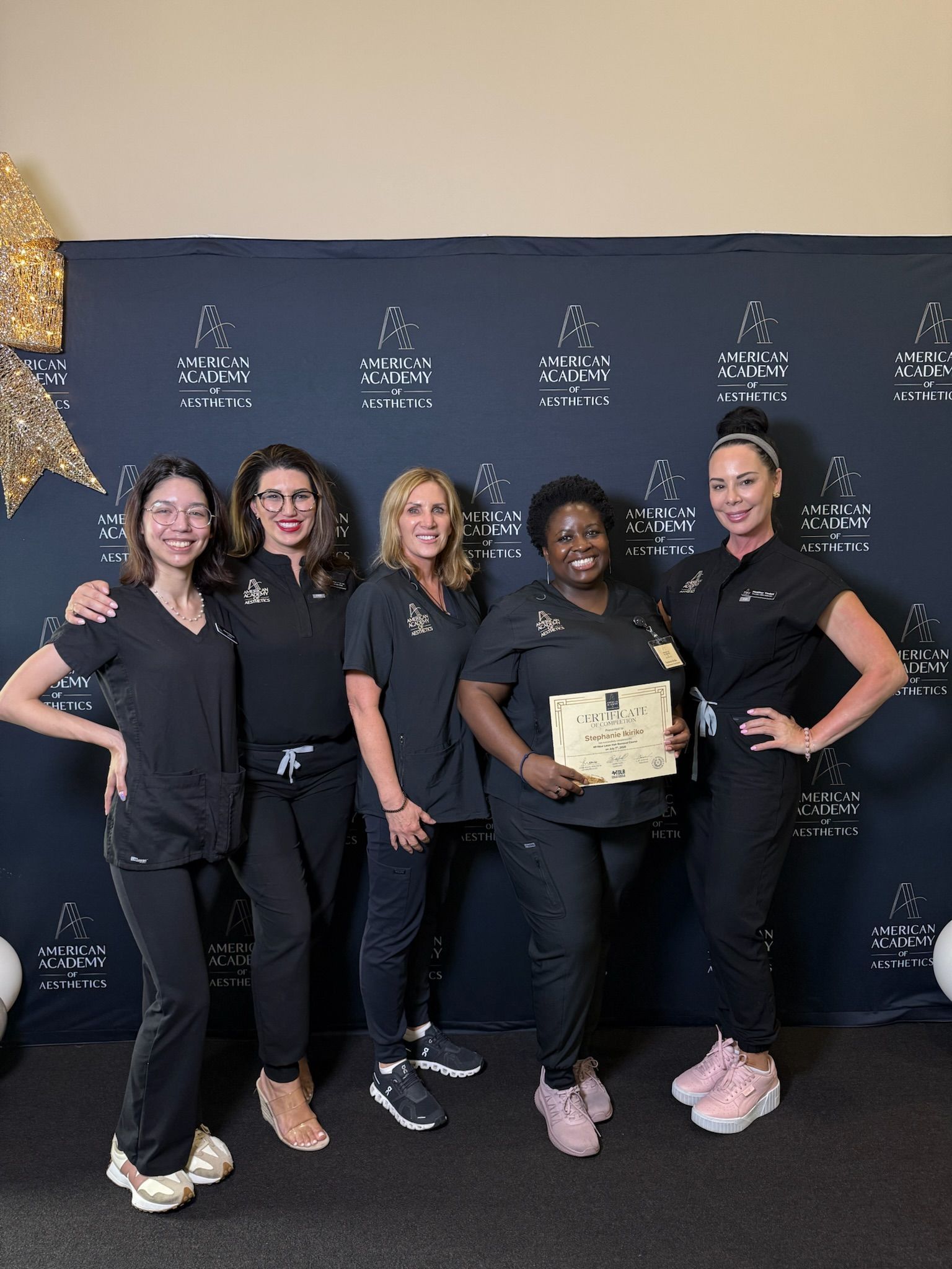 A recent aesthetics graduate holds her certificate alongside instructors at the American Academy of Aesthetics in Denton, TX.