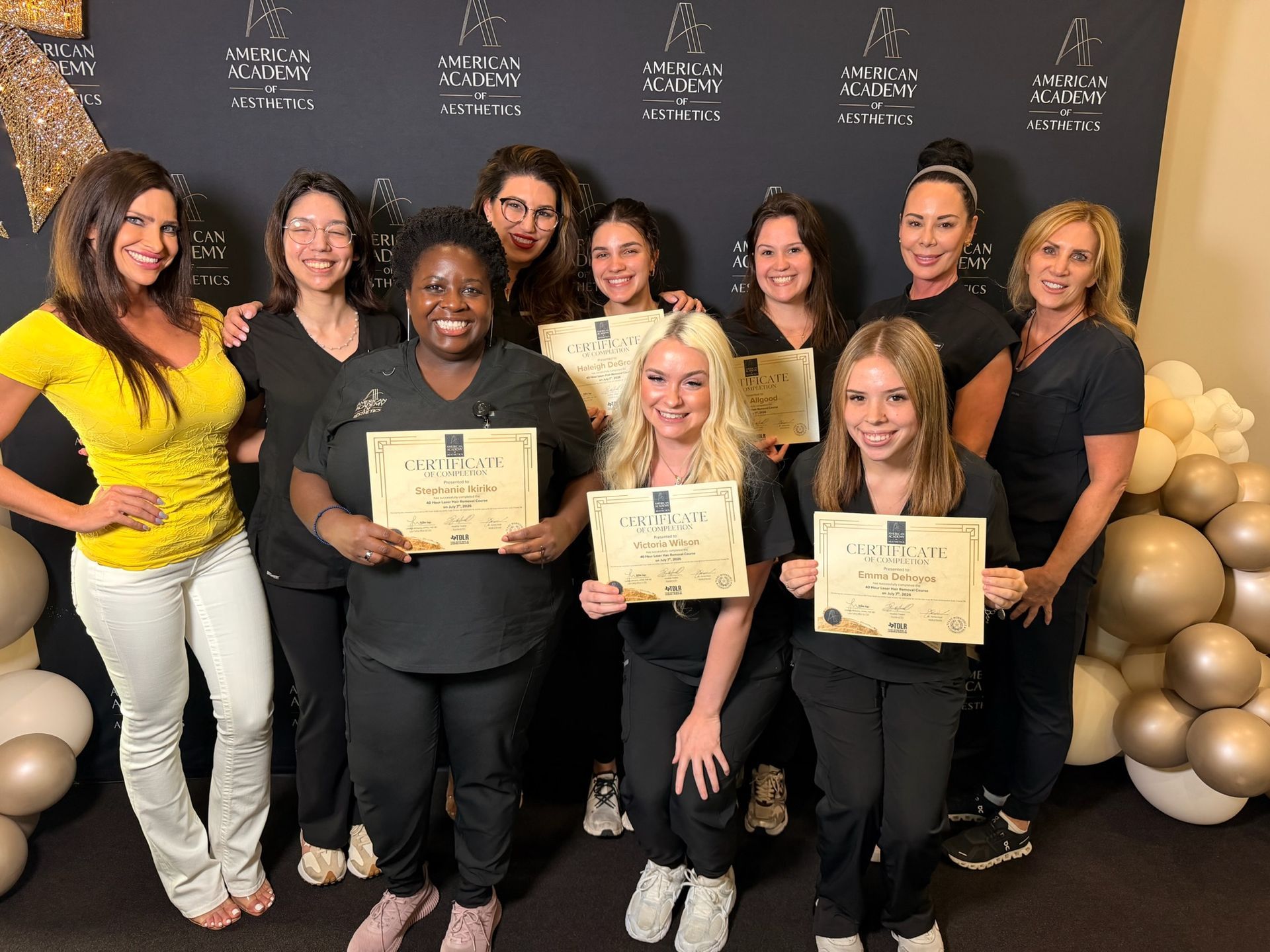 A group of recent aesthetics training graduates hold their certificates alongside instructors in Fort Worth, TX

