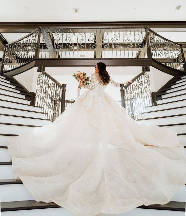 A bride in a long wedding dress is standing on a set of stairs.
