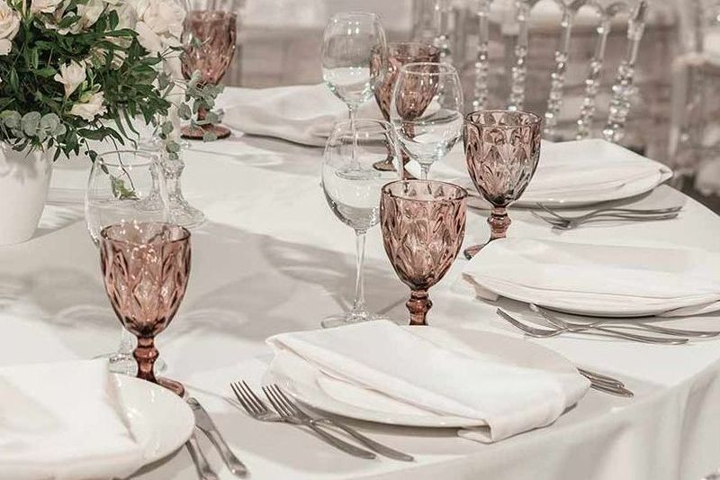 A table set for a wedding reception with plates , wine glasses , forks and knives.