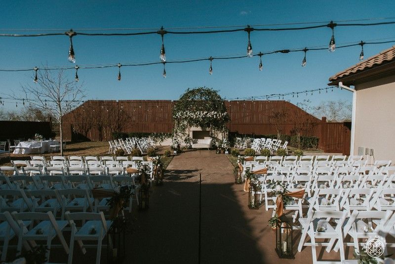 A row of white folding chairs are lined up in front of a building for a wedding ceremony.