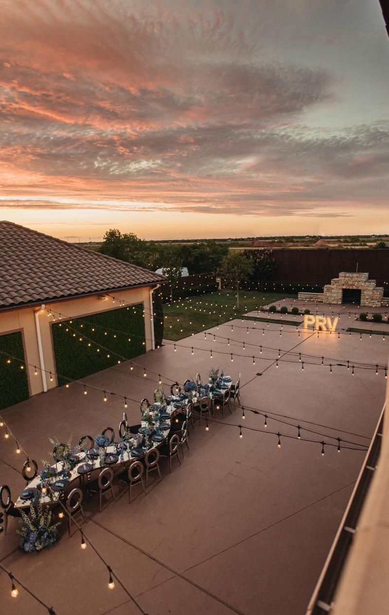 An aerial view of a long table and chairs in a courtyard at sunset.
