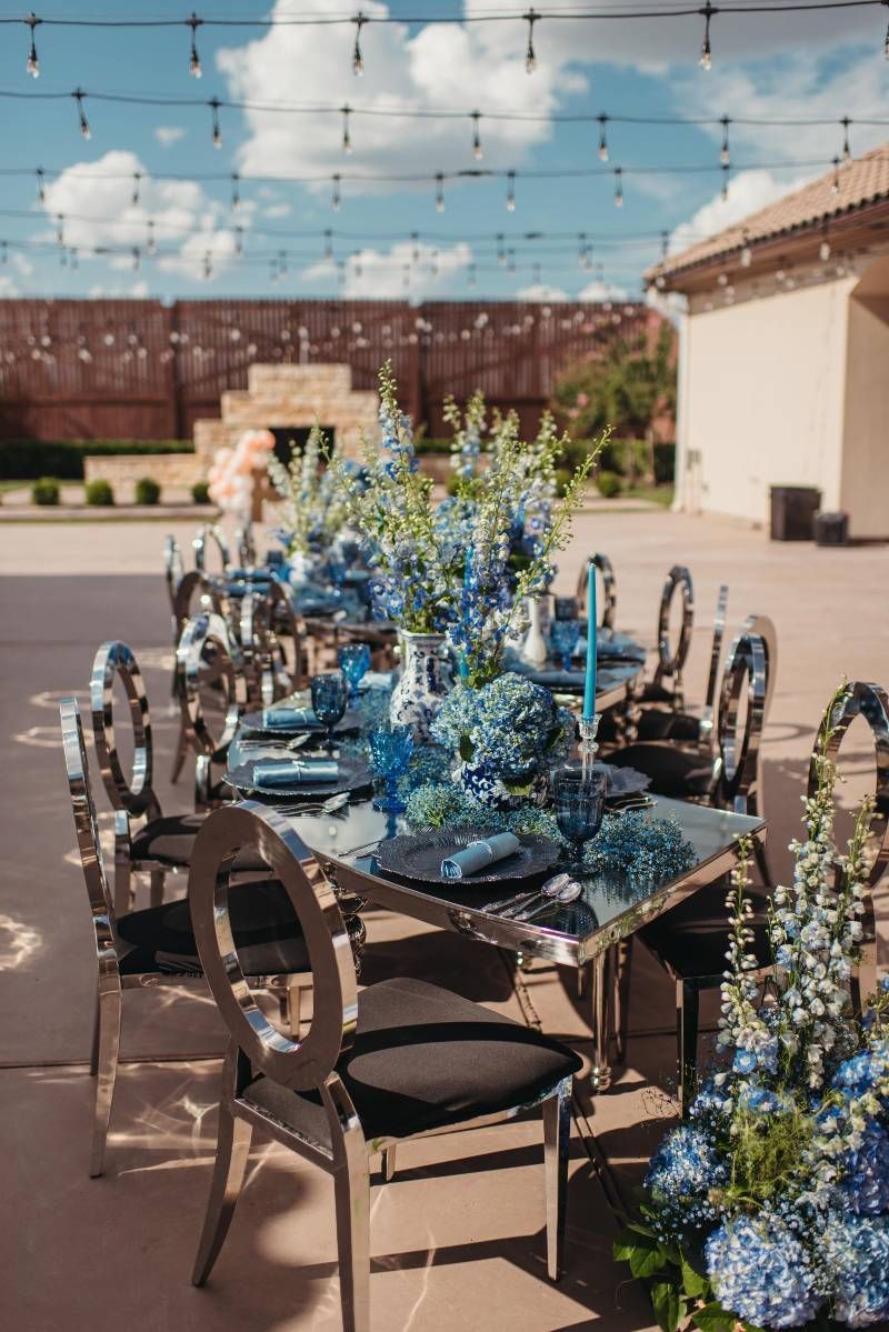 A long table with blue flowers on it is set for a wedding reception.