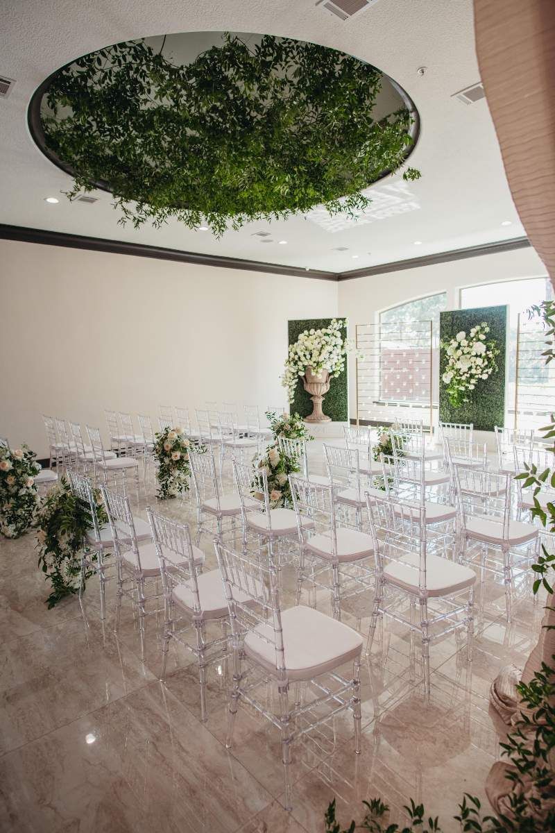 A room filled with clear chairs and flowers for a wedding ceremony.