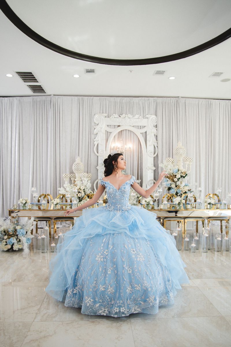 A woman in a light blue ball gown is standing in front of a table with flowers.