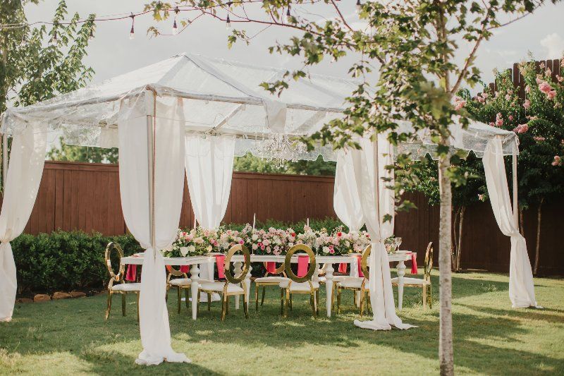 A clear tent with white curtains is sitting on top of a lush green field.