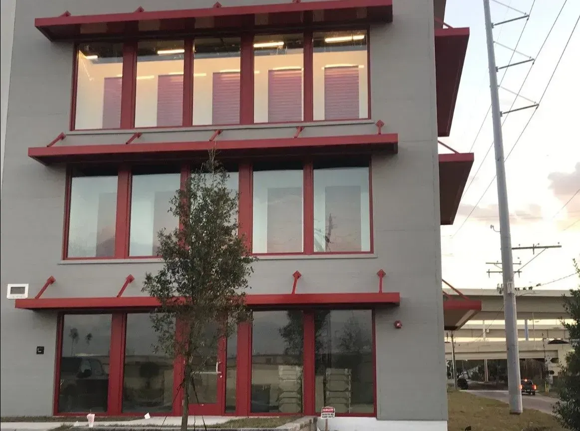 a gray building with red windows and a tree in front of it