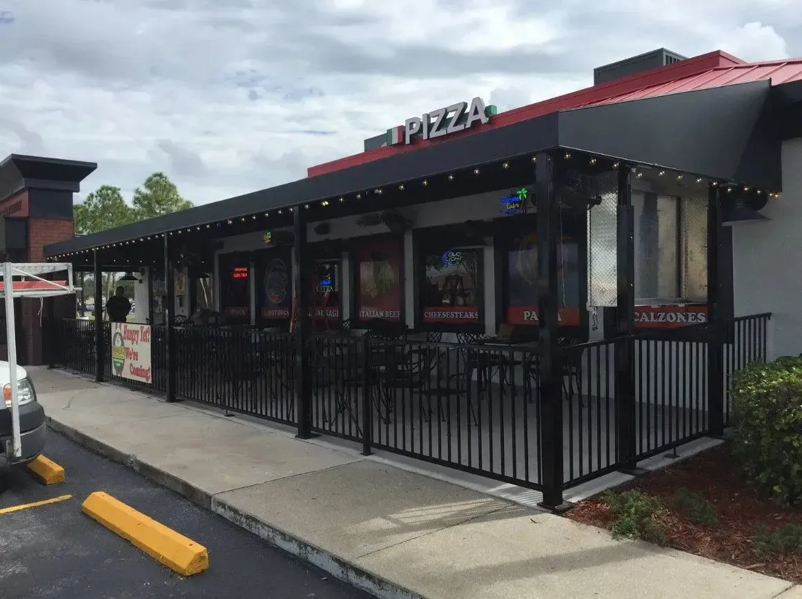a pizza restaurant with a fence around it and a parking lot in front of it .
