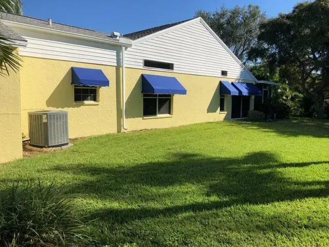 a yellow and white house with blue awnings on the windows