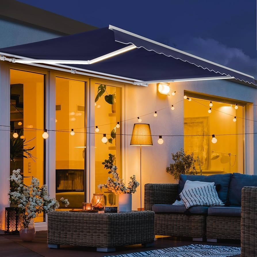 Outdoor patio with awning, string lights, wicker furniture, and potted plants at night.