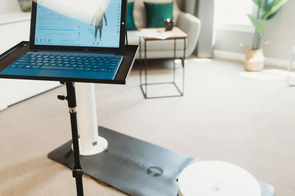 A tablet on a stand displaying a fitness program, positioned on a black exercise mat in a bright, modern living room.