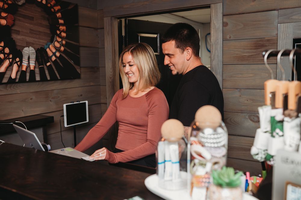 Smiling couple behind a counter in a cozy wooden cafe, with desserts and decor in the foreground