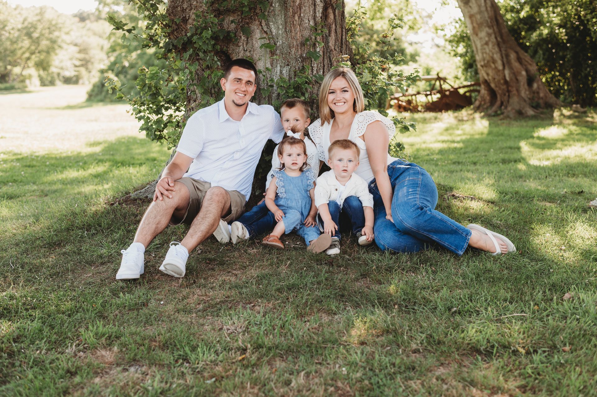 Woman and three young children seated on a large rock; outdoors. The woman smiles, holding a baby. Two boys wear green shirts.