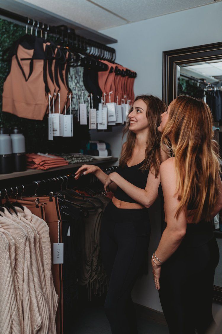Two women looking at clothing racks in a boutique. One smiles, the other looks on.