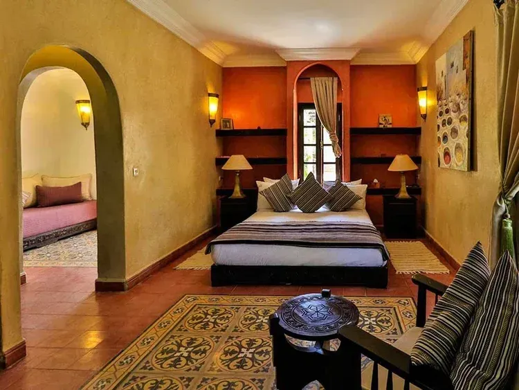 Bedroom with bed, nightstands, rug, arched doorway, and decorative elements; warm colors.