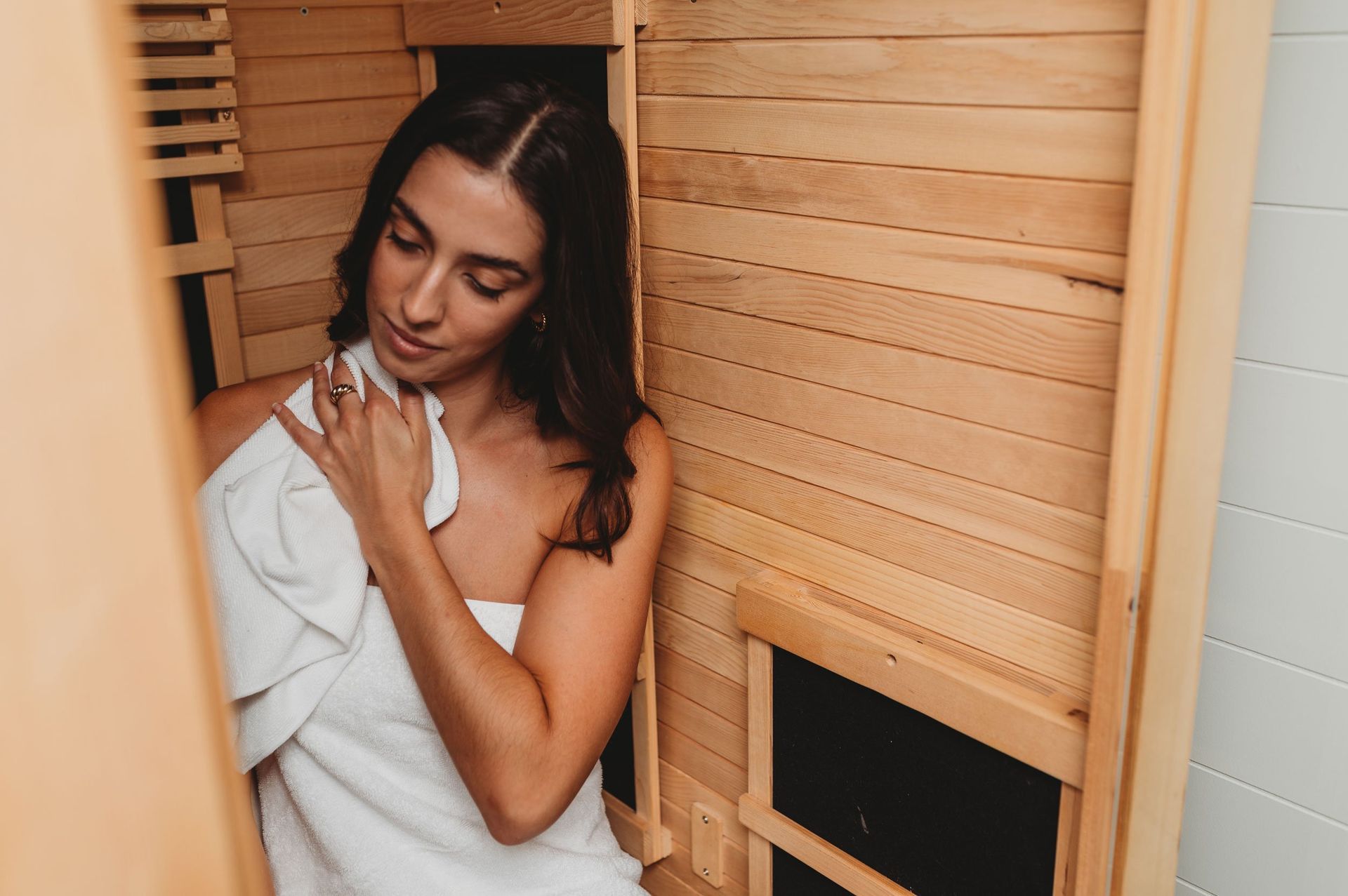 Woman wrapped in a towel, emerging from a wooden sauna, looking relaxed.