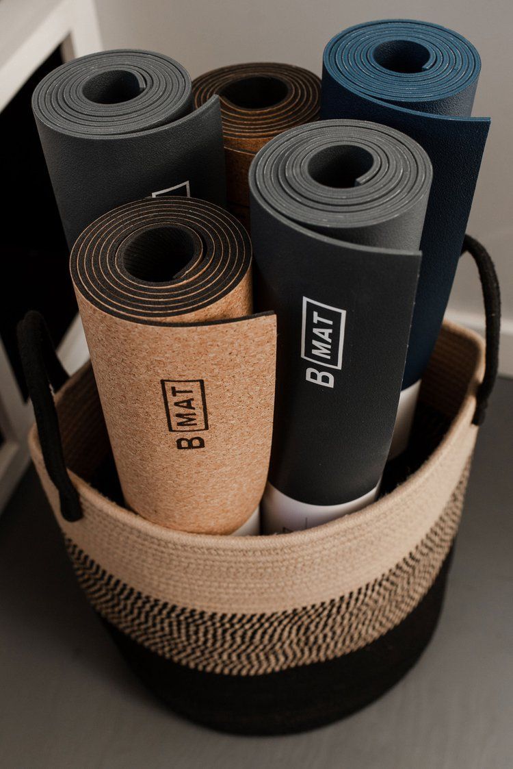 Rolled yoga mats in a basket; cork and dark blue, black, and gray mats.