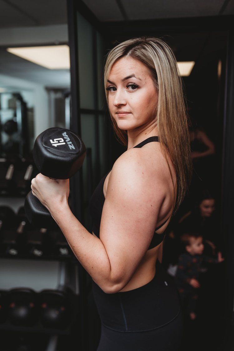 Woman lifting a dumbbell in a gym; she looks to the camera.