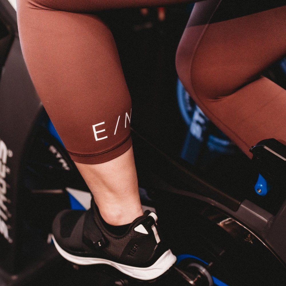 Person's legs in brown cycling gear on a stationary bike, showing a shoe and the
