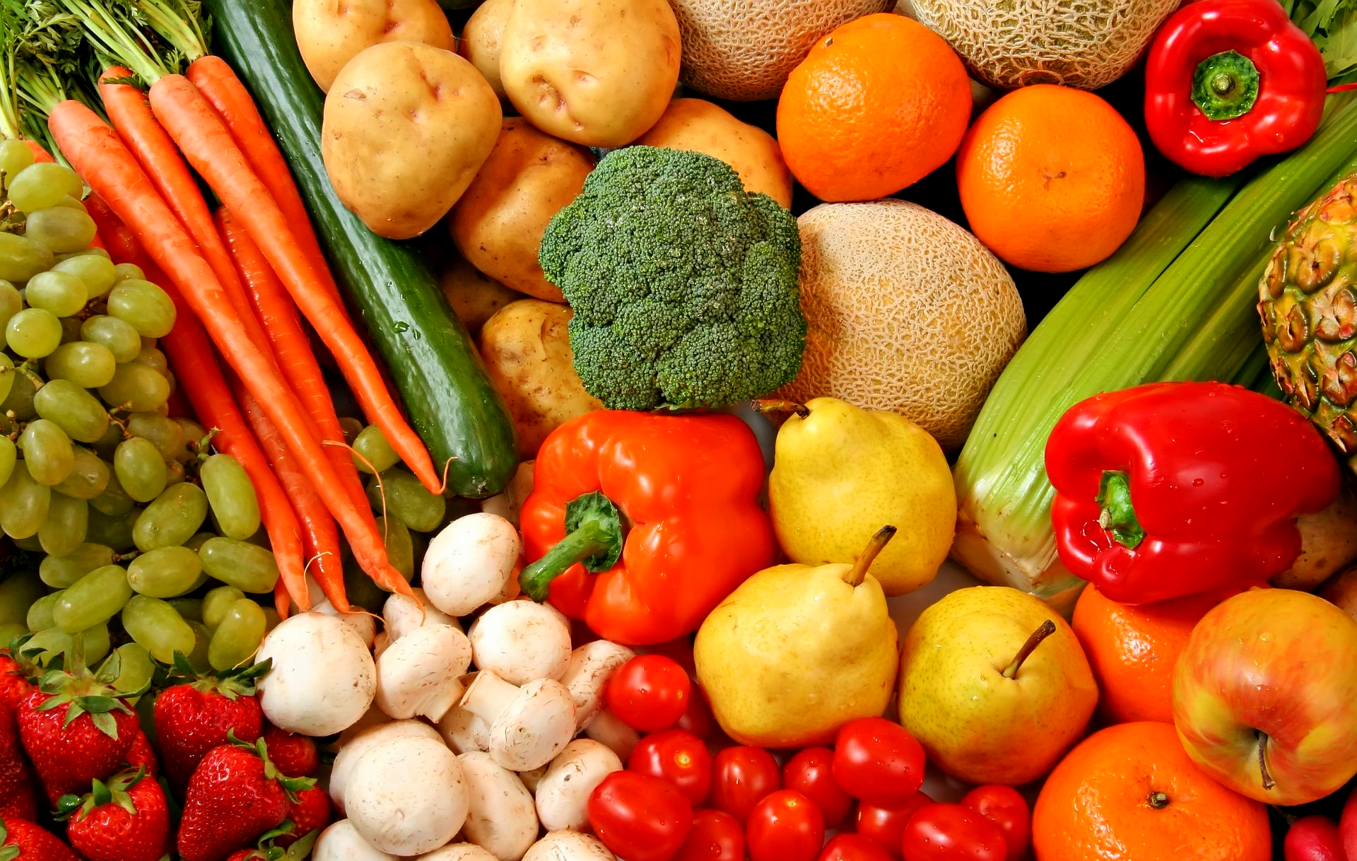 Pile of colorful fruits and vegetables: grapes, carrots, oranges, peppers, broccoli, and more.