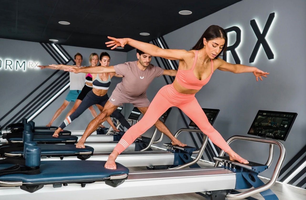 People exercising on treadmills in a modern gym, stretching with arms extended on black equipment.