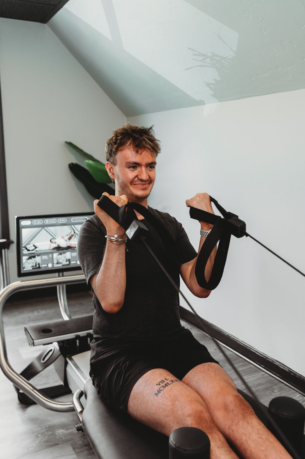 Person using a rowing machine indoors, pulling black handles and smiling.