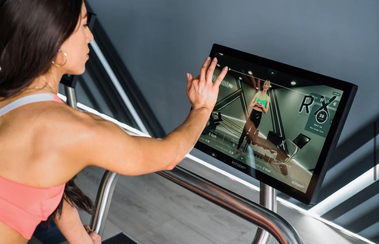 Woman in gym exercises with a kettlebell; baby watches nearby.