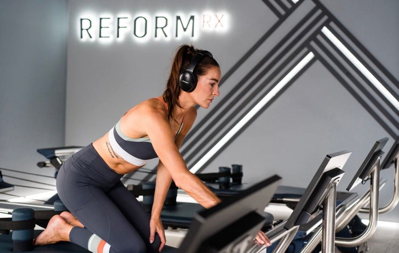 Women in black activewear selecting dumbbells in a gym.