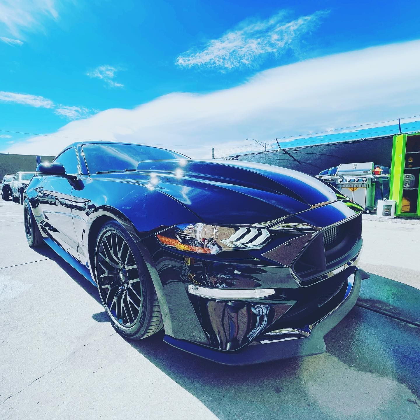 Black sports car parked outdoors under a bright blue sky at a gas station