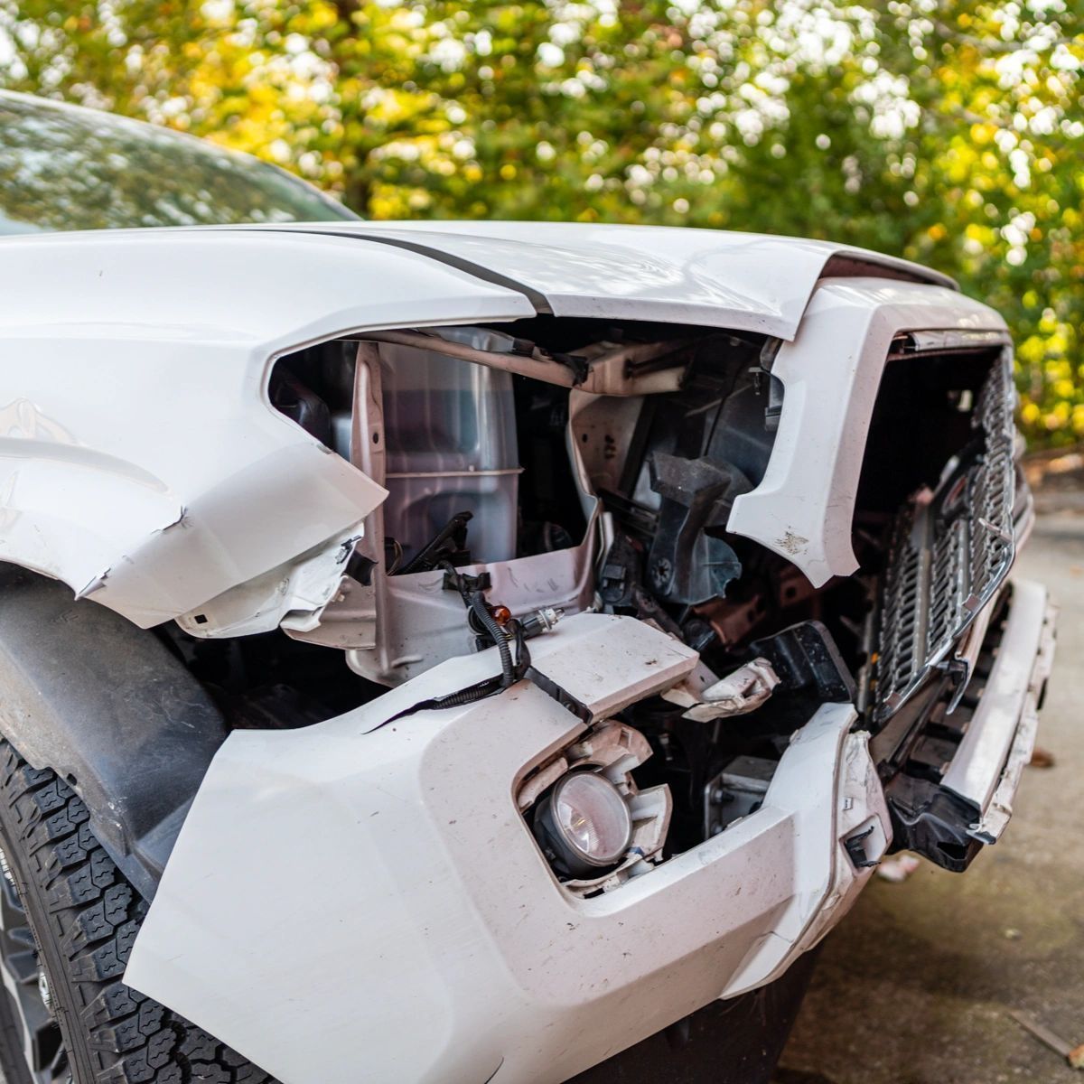 White SUV with severe front-end collision damage and exposed engine parts outdoors