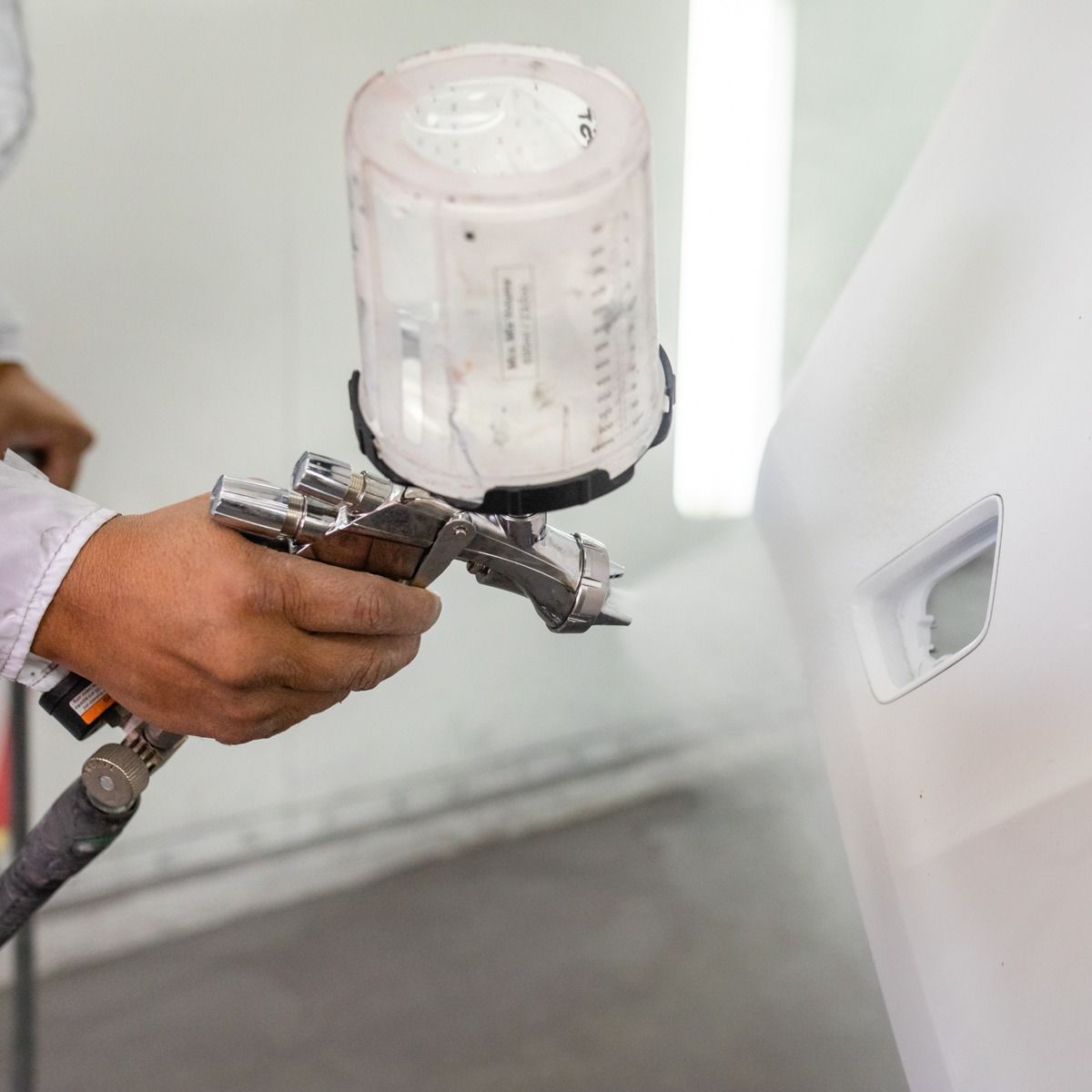 Hand spraying white paint onto a vehicle panel with a paint gun