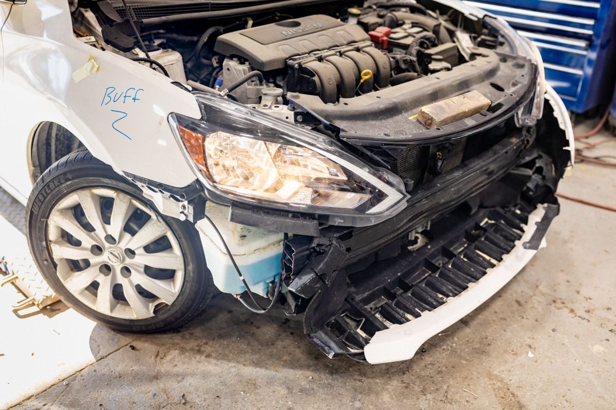 Damaged white car with front-end collision and exposed engine in a repair shop