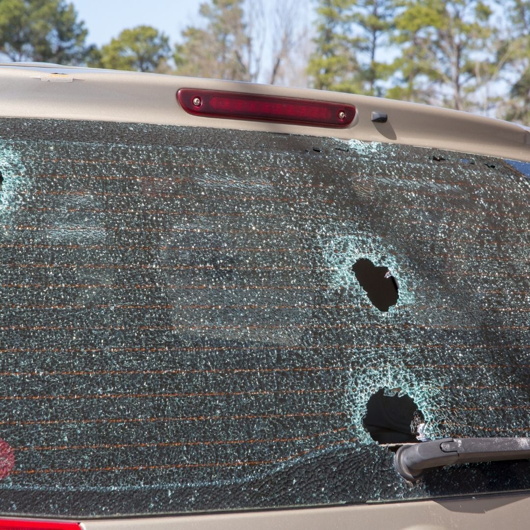Shattered rear car window with two bullet holes and broken safety glass