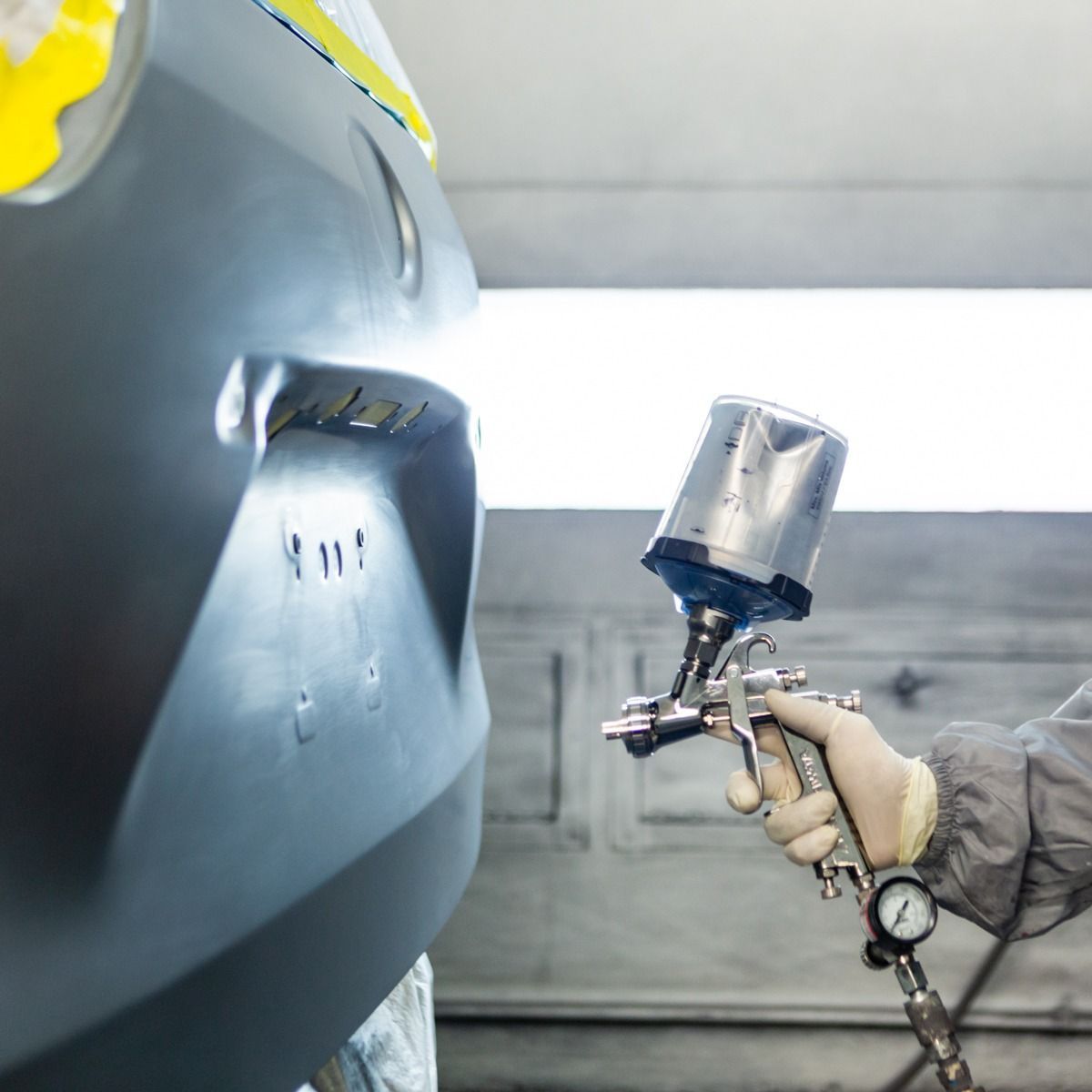 Spray-painting a gray metal surface with a handheld spray gun in an industrial setting