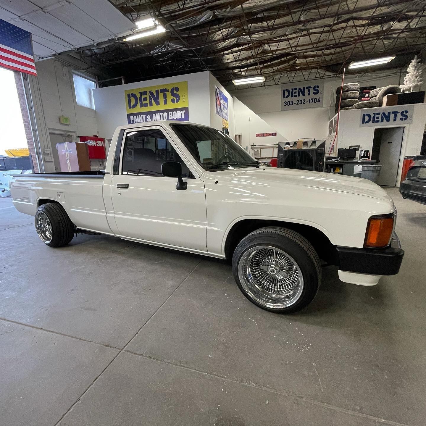 White vintage pickup truck in an auto shop garage with DENTS signs in the background