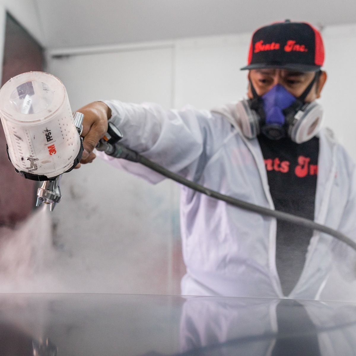 Worker in white protective gear spray-painting a surface with a paint sprayer and respirator mask