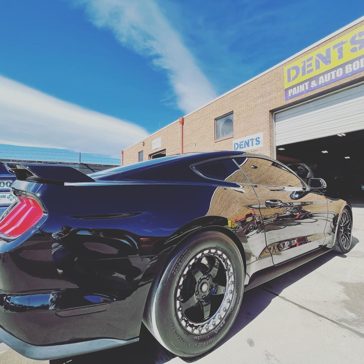 Black sports car parked outside a repair shop on a sunny day