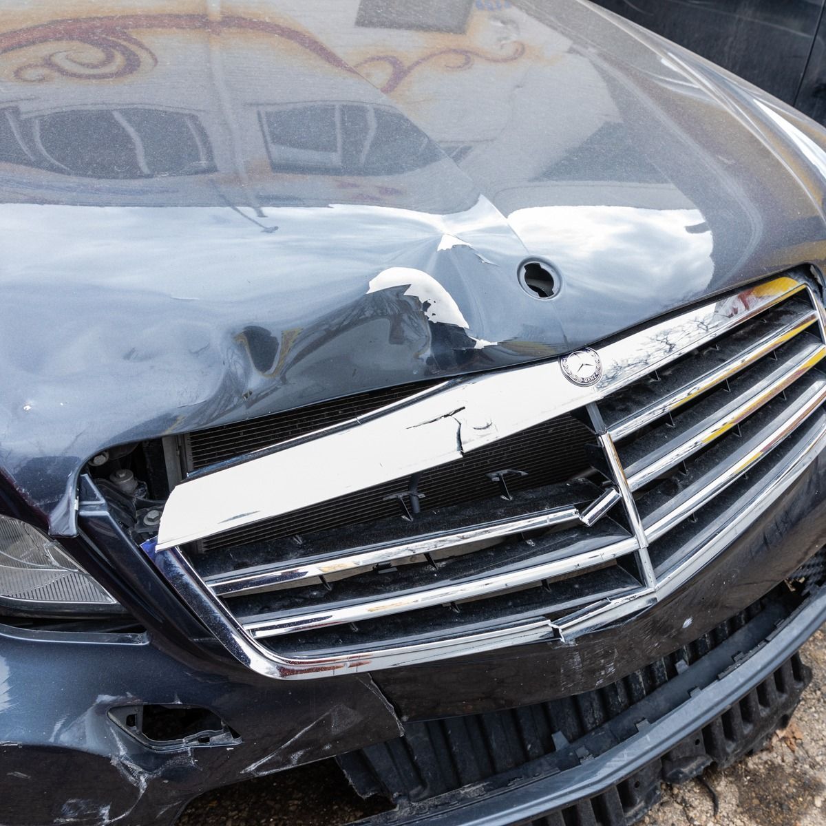 Damaged black car front with crumpled hood, broken grille, and dented bumper after a collision