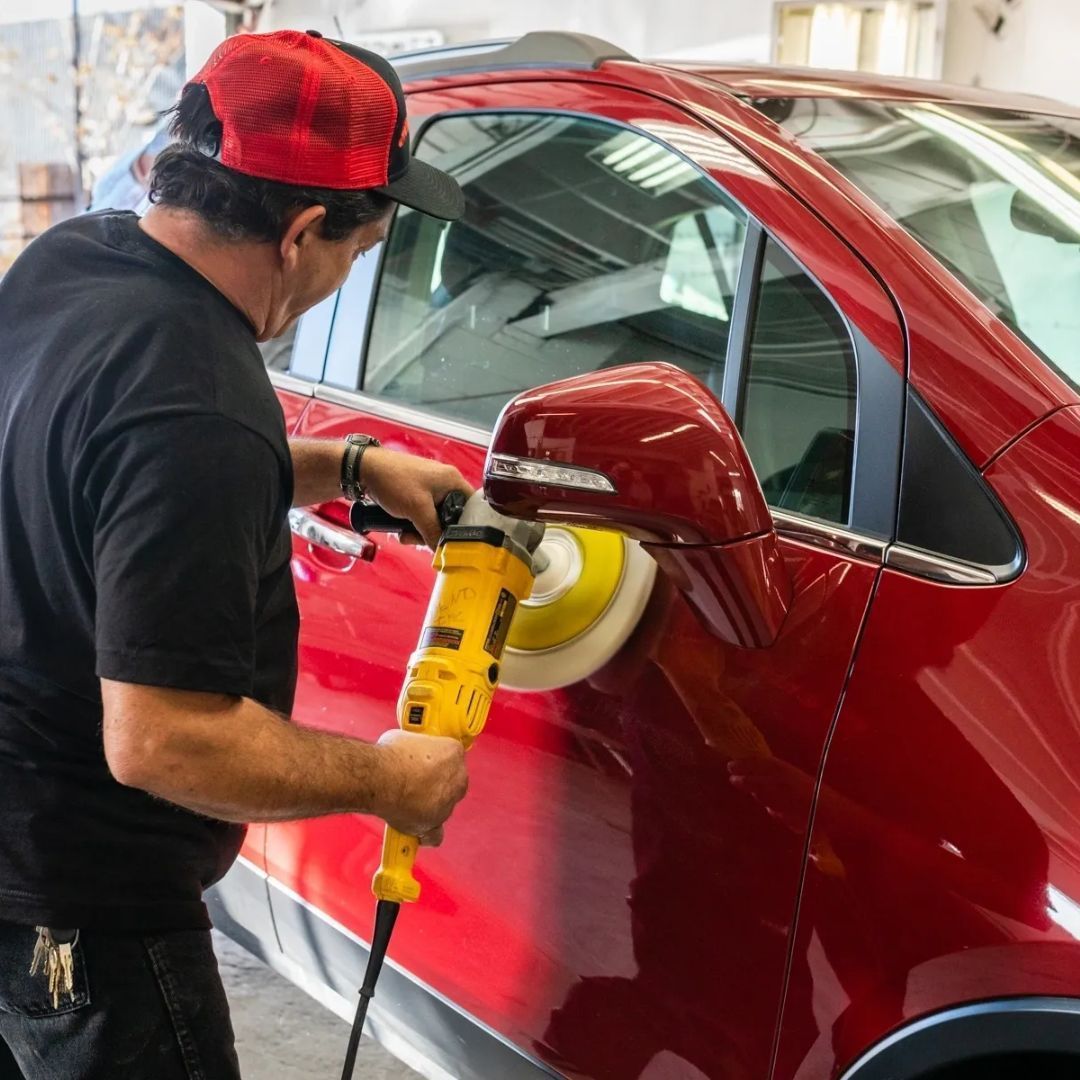 Worker polishing a red car door with a buffer in an auto shop