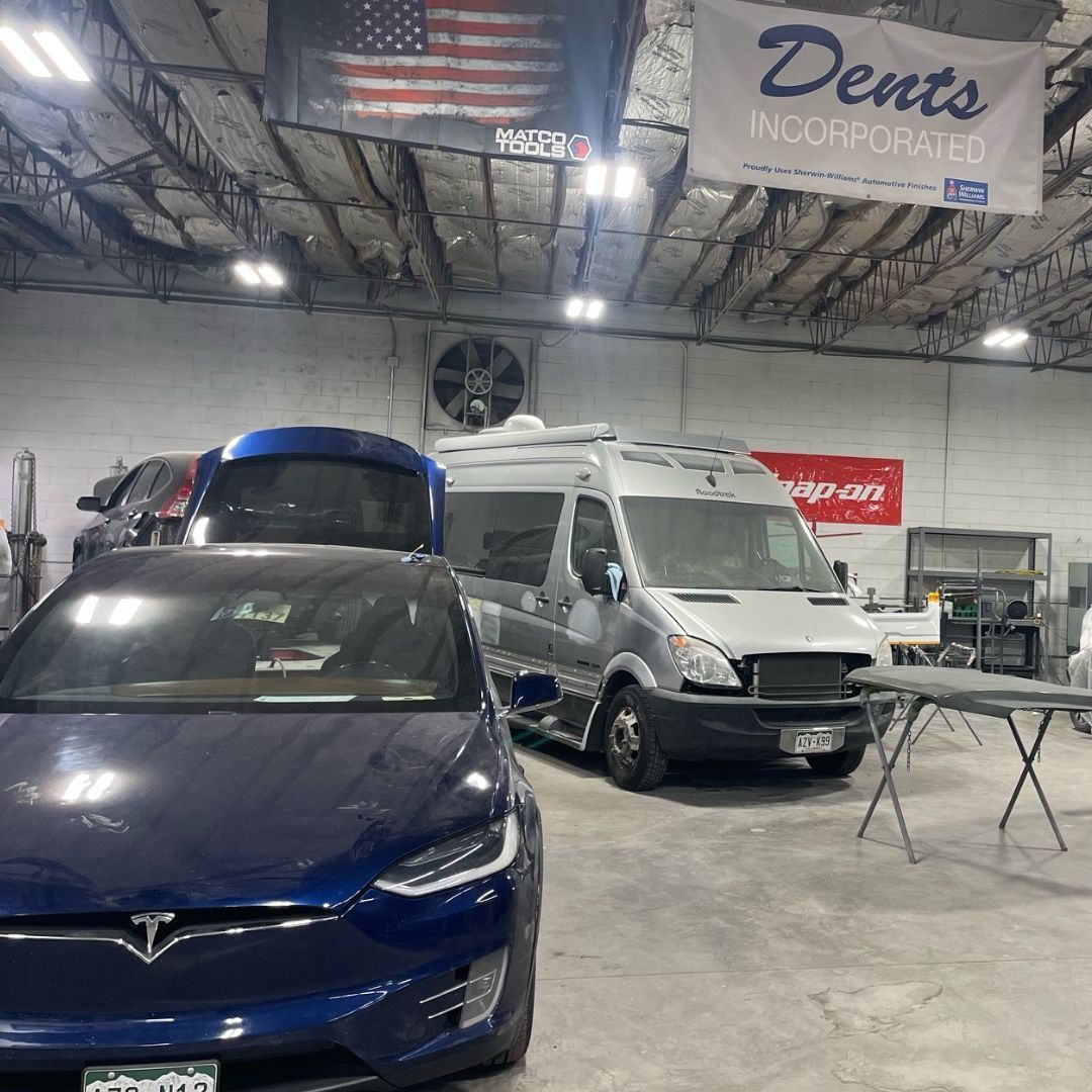 Blue Tesla and white van inside an auto shop with a “Dents” sign overhead.
