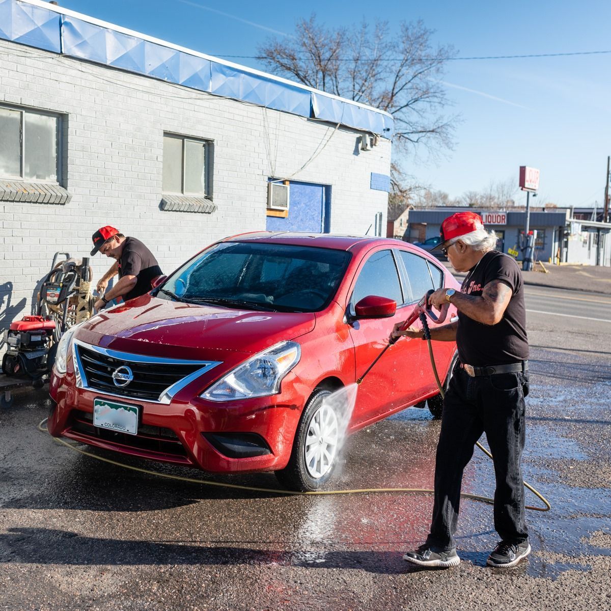 Car wash scene with a red SUV being sprayed by workers in Santa hats near a white building.