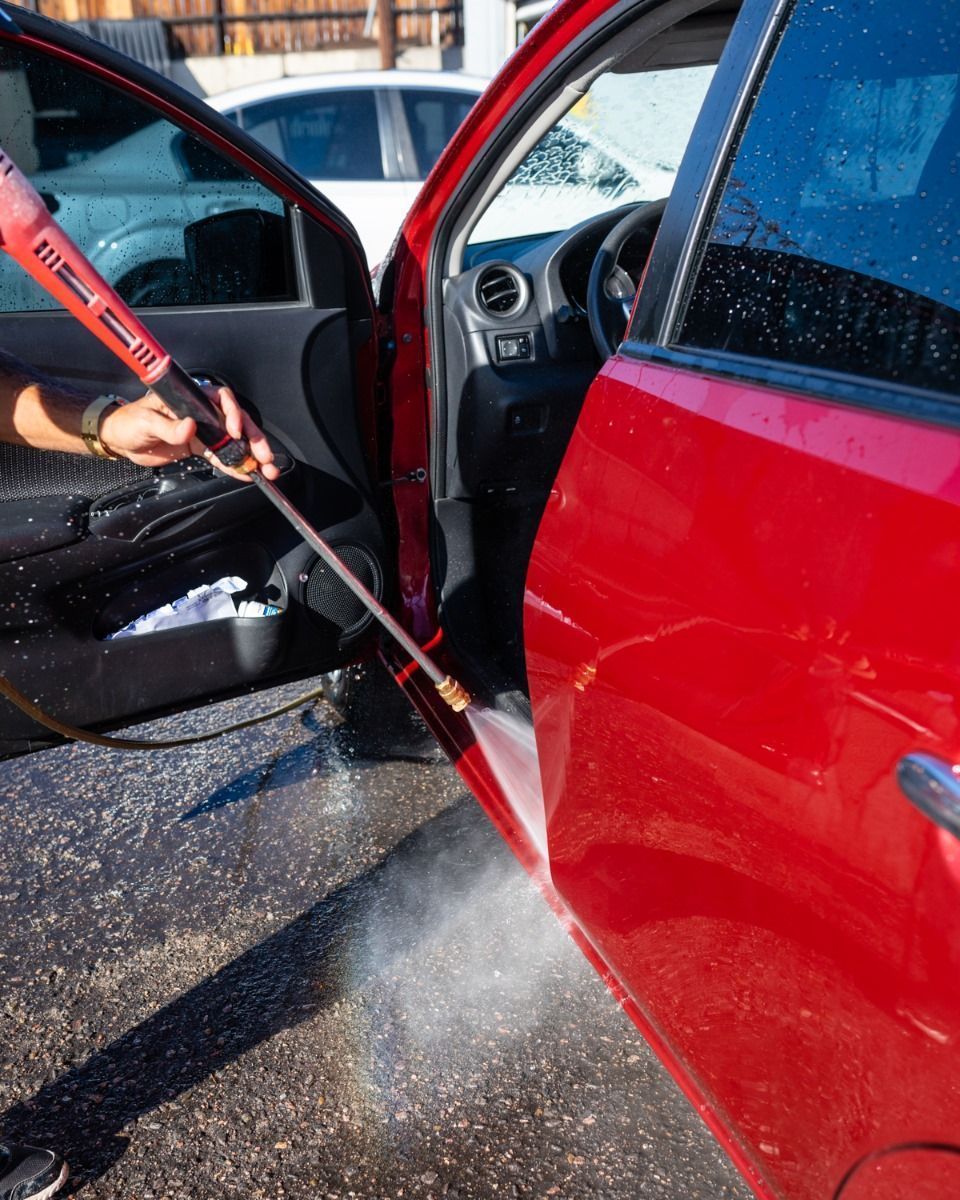 Person pressure-washing the open door and side of a red car outdoors