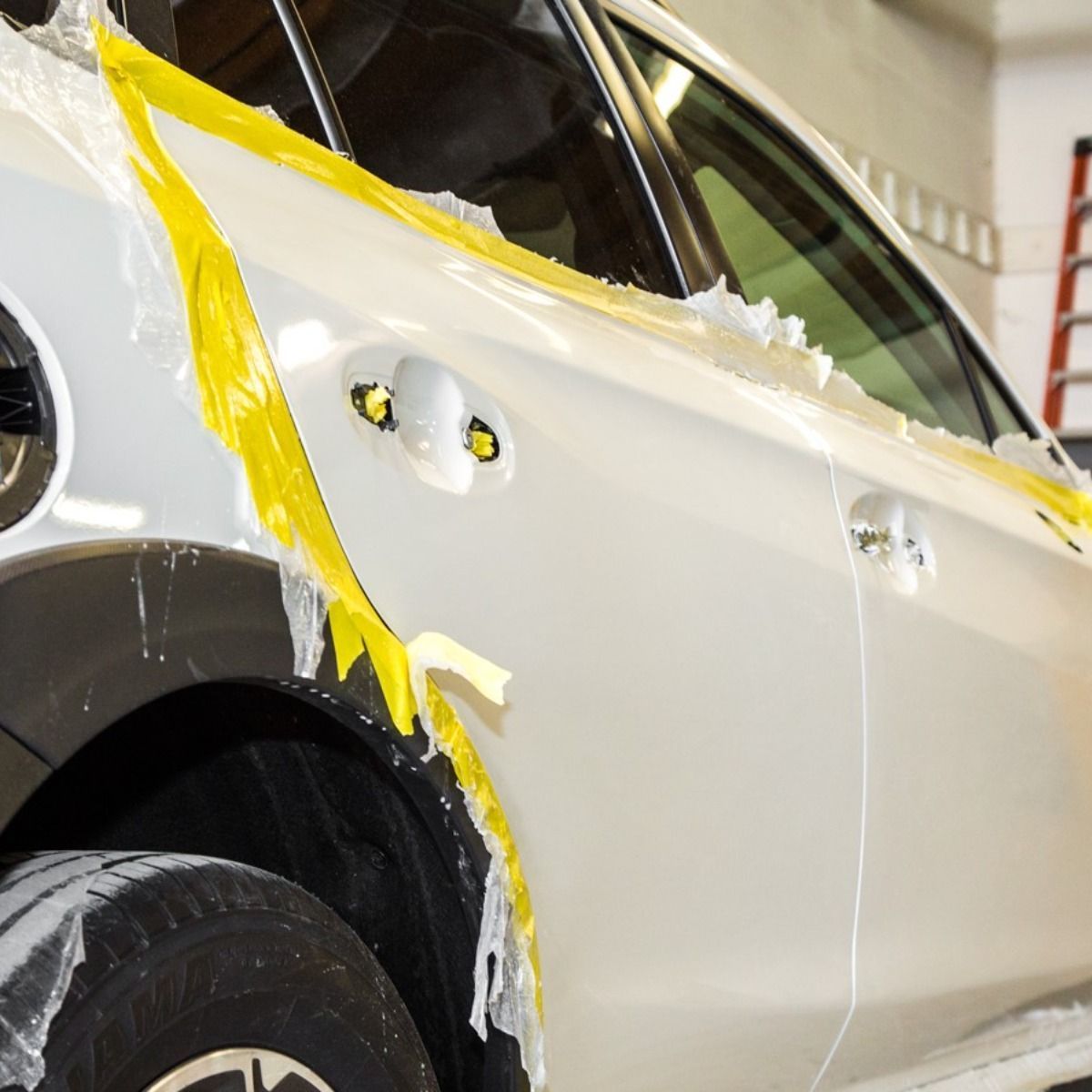 Silver car under repair in a body shop, with yellow masking tape and white filler on the rear quarter panel