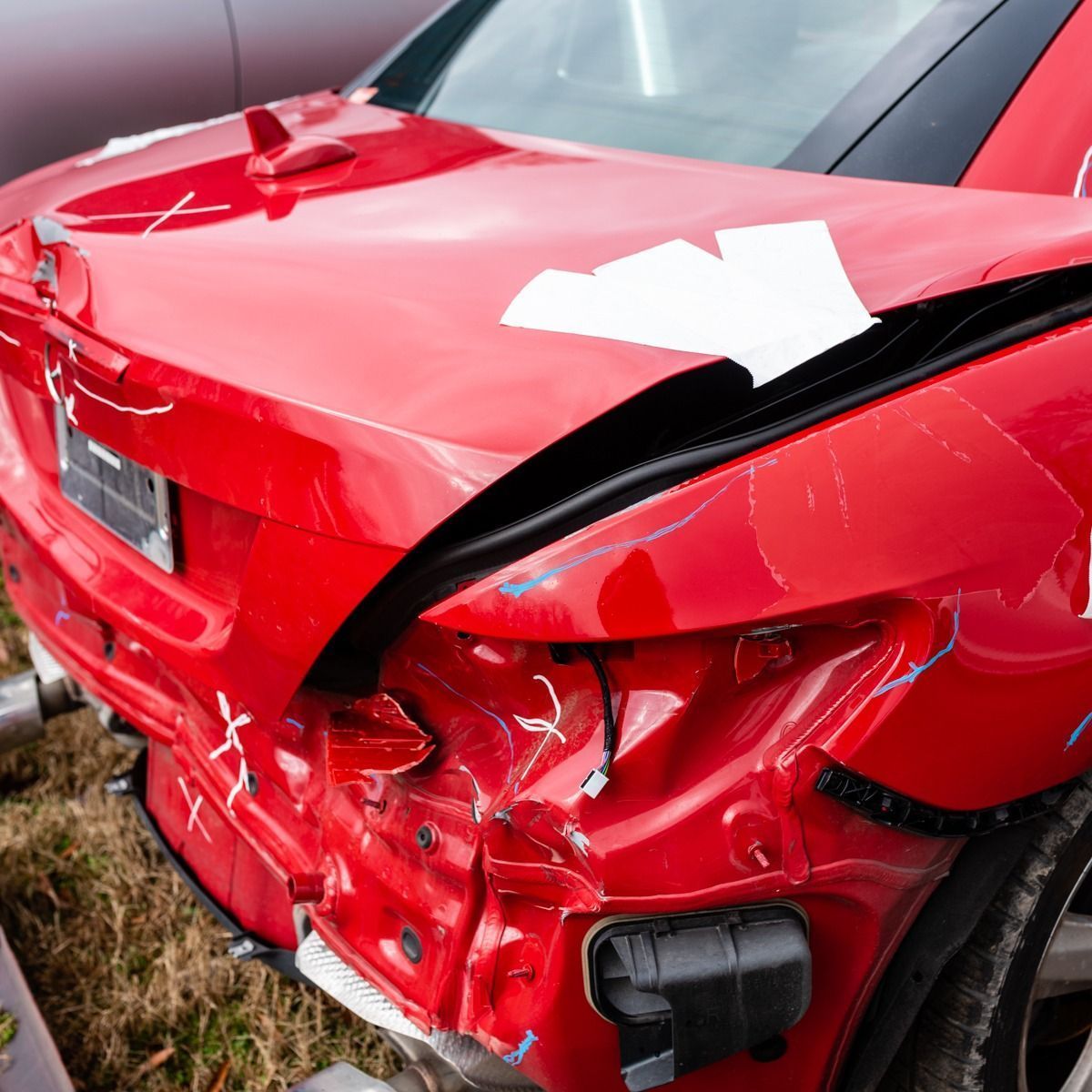Severely damaged red car rear after a crash, with a crushed trunk and torn bumper