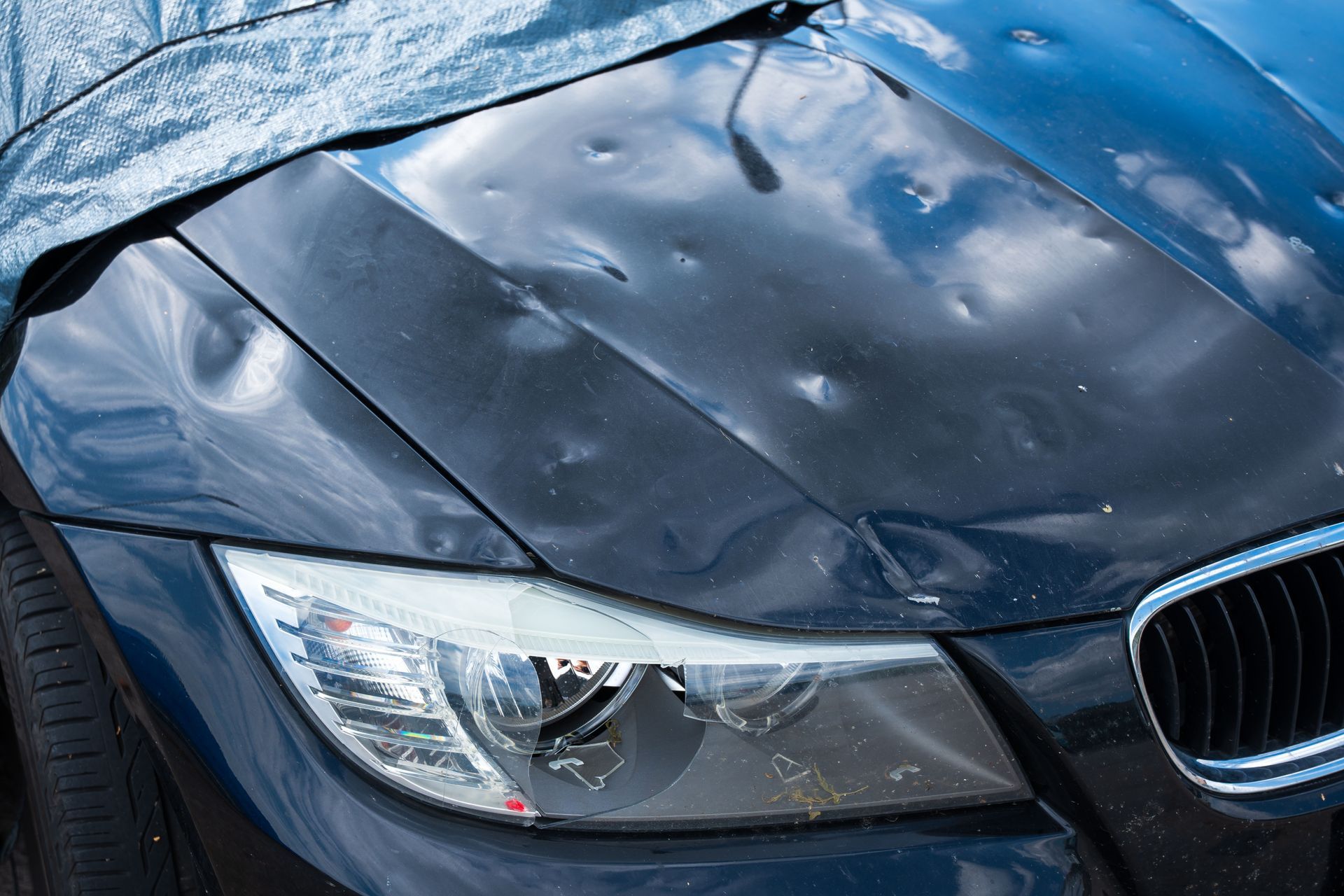 Close-up of a wet blue car hood and headlight with raindrops and a visible grille