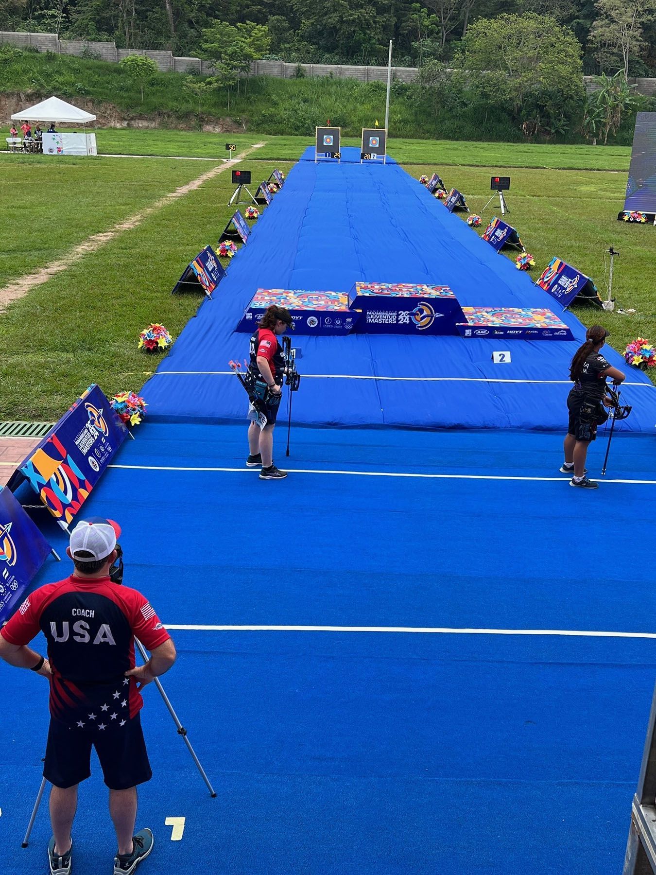A man wearing a usa shirt is standing on a blue mat in a field.