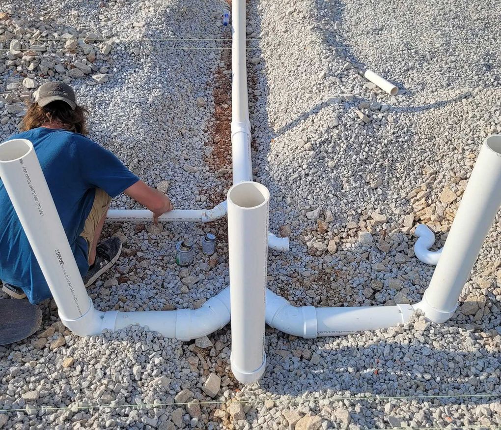 Person assembling PVC pipes on gravel ground.