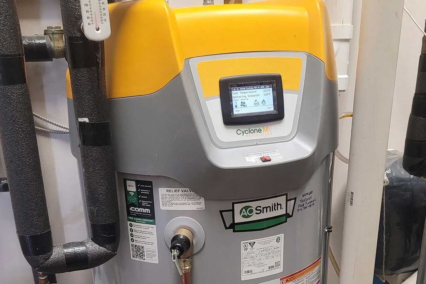 A cylindrical water heater with a yellow and gray top, display screen, and black insulated pipes.